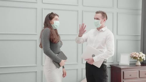 Young american business man and woman in face mask greeting with elbow bump at office.