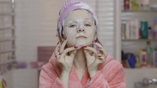 Woman Applying Cosmetic Face Mask in Bathroom. Skincare Spa. Facial Mask