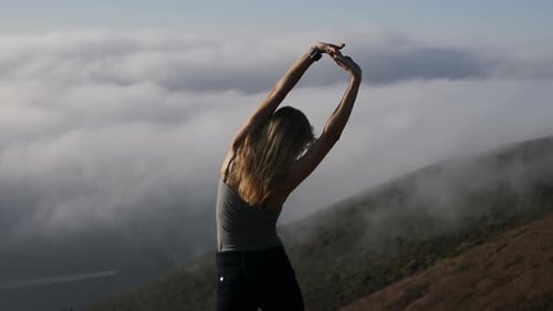 Woman Stretching on a Mountain Above the Clouds