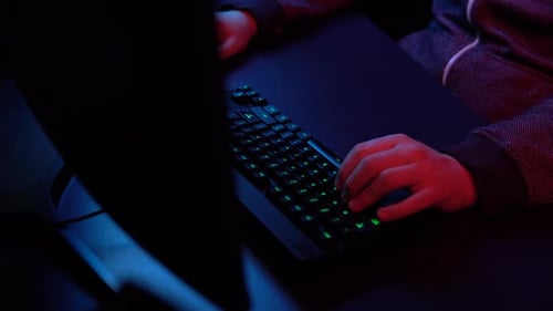 Ein junger Mann spielt Computer. Hände arbeiten an der Tastatur Nahaufnahme. Blaues und rotes Licht fällt auf