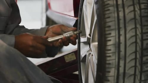 African American male car mechanic screwing a wheel to a car with a wrench