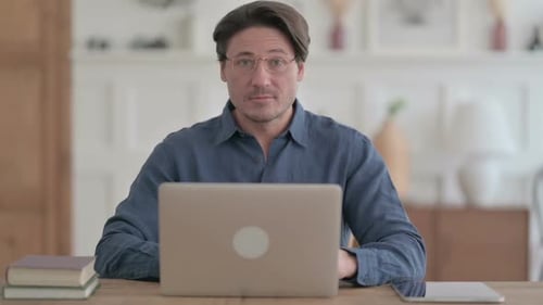 Young Man Showing Thumbs Up Sign While using Laptop in Office