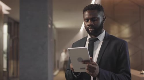 Black Man in Suit Using Tablet in Lobby of Hotel