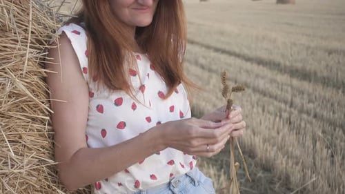 Woman Resting with Wheat on Hay Bale in Field