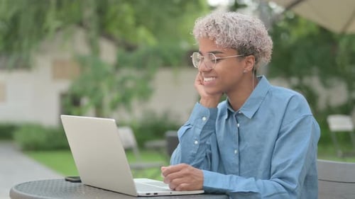 Young African Woman Doing Video Chat on Laptop in Outdoor Cafe