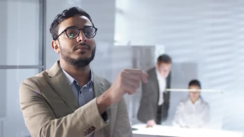 Arab Businessman Using Invisible Multi-Touch Screen on Glass Wall in Office