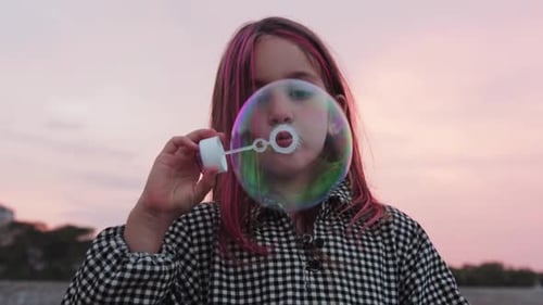 A Little Girl with Pink Strands Blowing Soap Bubbles