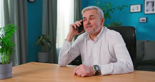 Älterer grauhaariger 55er Mann sitzt zu Hause und hält Smartphone Genießen Sie ein angenehmes Gespräch