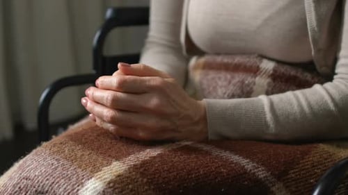 Woman Nervously Kneading Numb Cold Hands Sitting in Wheelchair, Feeling of Doom