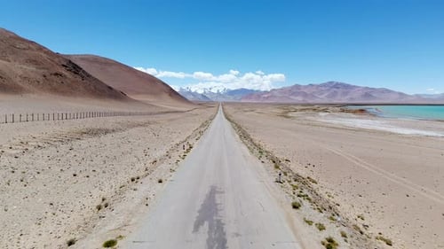 Aerial View of Dirt Road Crossing Desert Beside Blue Lake Around Sand Dune and Mountain