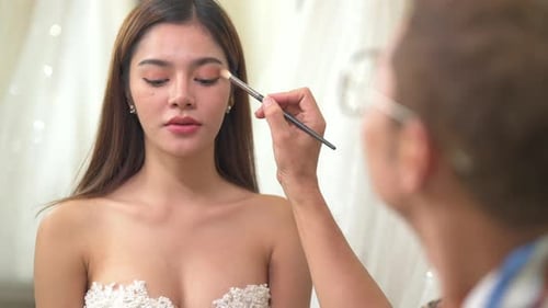 4K Asian LGBTQ guy make-up artist applying makeup to female bride customer at wedding studio.
