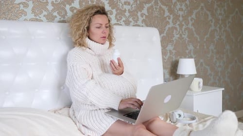 Pregnant Woman Taking Pills in Bed with Laptop