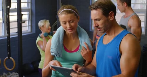 Man and Woman Review Fitness Plan on Tablet at Gym