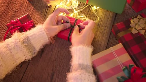 close-up asian female hand tying a bow ribbon on a box with a gift on a wooden table