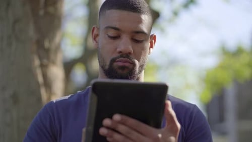 Afro-American Muscular Man on Bench in Park Typing on Tablet