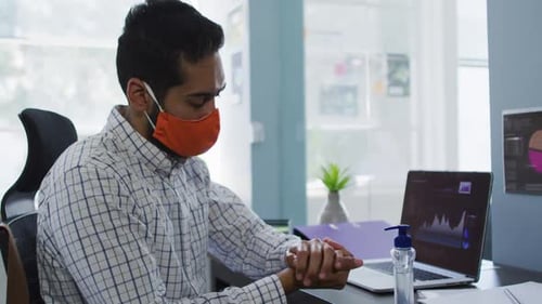 Middle eastern man wearing face mask using hands sanitizer at modern office