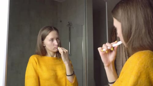 Young Woman Brushing Teeth in Bathroom Mirror
