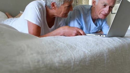 Senior Couple Relaxing on Bed with Laptop