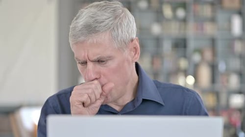 Man Coughing While Working on Laptop in Office