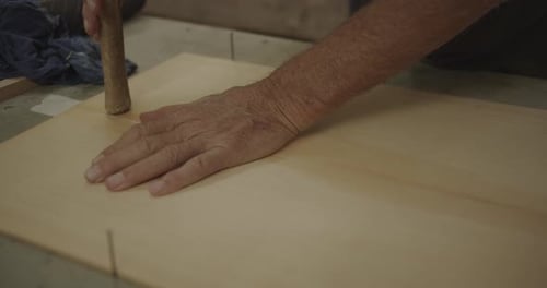 Old hands tap a hammer over glued wood