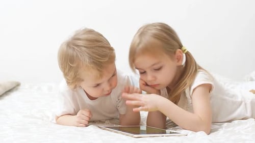 Brother and Sister Playing with Tablet on Bed