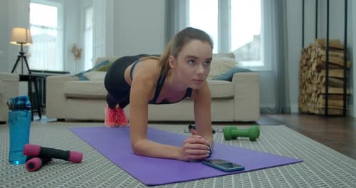 Frau in athletischer Trainingskleidung macht eine Plankenübung, während sie eine Stoppuhr auf ihrem Handy benutzt
