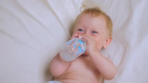 Baby girl drinking water from bottle. Nutrition for babies.