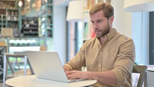Professioneller junger Mann benutzt Laptop im Café