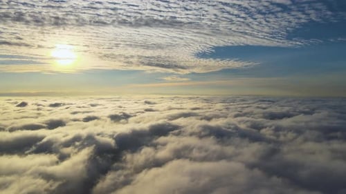 Aerial view of vibrant yellow sunrise over white dense clouds with blue sky overhead.