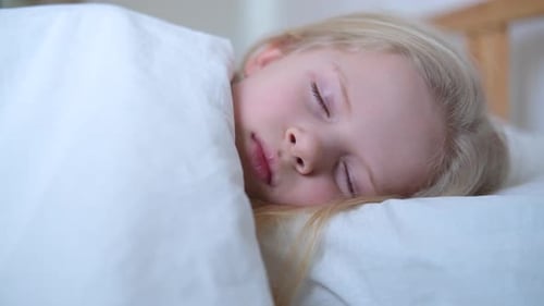 Sleeping Little Blonde Girl Close Up in Big Bed with White Bedding Early in the Morning