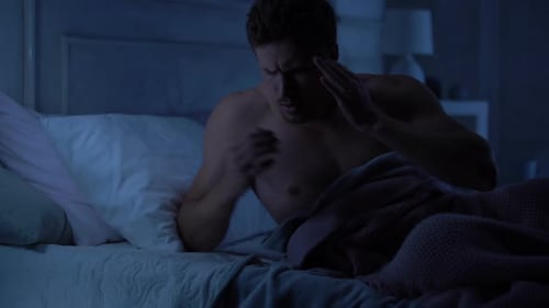 Young Man Lying in Bed With a Headache