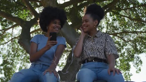 Two mixed race women listening music in park
