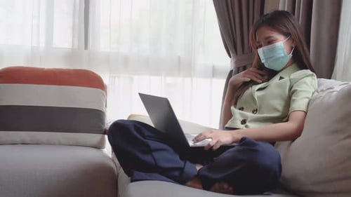 Happy young asian woman in protective mask using laptop to video call or facetime to talk friend