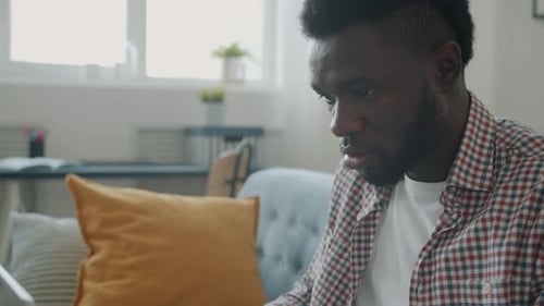 Young Man Working on Laptop from Home on Sofa