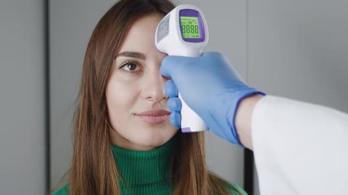 Closeup of a Doctor's Hand in a Medical Gown Holding a Noncontact Infrared Thermometer Over the