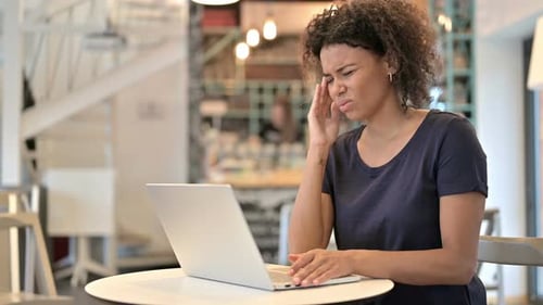 Young African Woman with Headache Using Laptop in Cafe