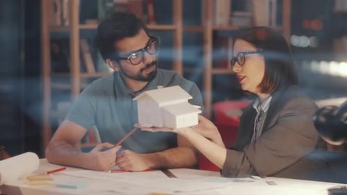 Male and Female Architects Discussing House Mockup Model in Office