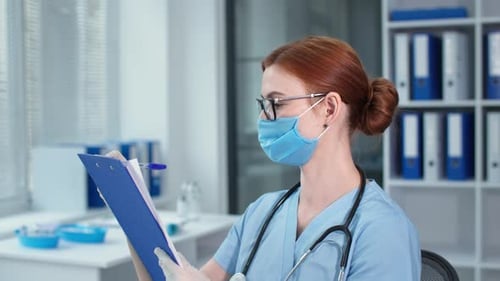 Portrait of Beautiful Female Doctor in Blue Uniform with a Stethoscope Writes Notes in Clipboard