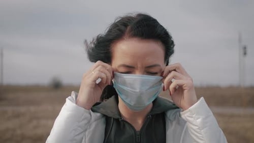 Woman Puts on Surgical Mask in Rural Setting