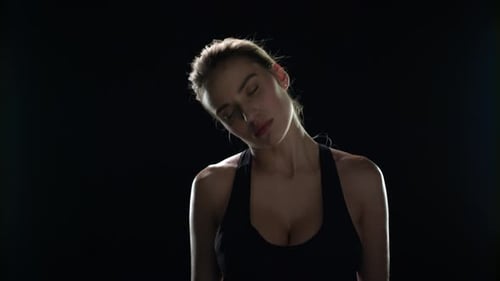 Woman Does Neck Stretches Against Black Background