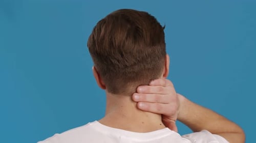 Back View Shot of Man Massaging His Inflamed Neck Blue Studio Background Slow Motion