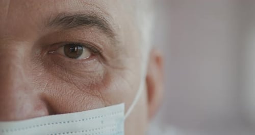 Male Doctor or Nurse in Uniform, Mask Looking Straight at Camera. Close Up of Eye. Slow Motion