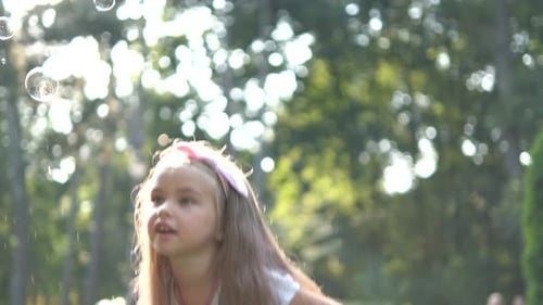 Little happy child girl cathing and bursting soap bubbles outdoors in summer.
