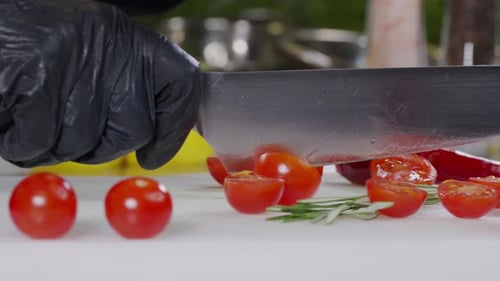 Chef Takes Cherry Tomatoes Cuts Vegetable Into Halves with Kitchen Knife on Dark Cutting Board