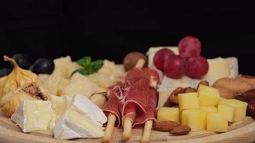 Préparation de l'assiette de fromages : parmesan, raisins, miel, noix, grissini, jambon, prosciutto