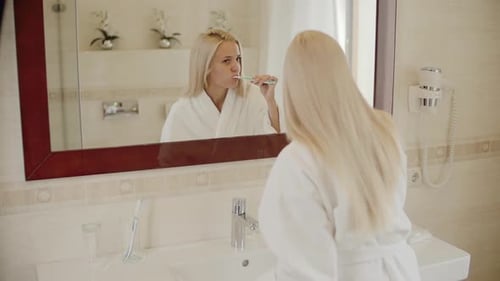 Woman Brushing Teeth in Bathroom Mirror