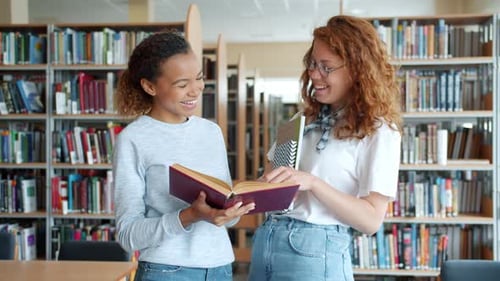 Cheerful Girls Students Chatting in Library Discussing Book Laughing