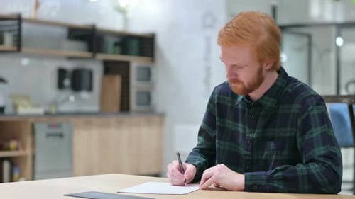 Young Beard Redhead Man Writing on Paper in Cafe