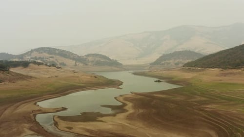 Slow tracking drone shot flying over a mostly dry Emigrant Lake in Southern Oregon, showing smokey d