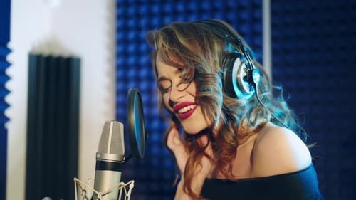 Young woman recording a song in a professional studio. The girl sings into the microphone.